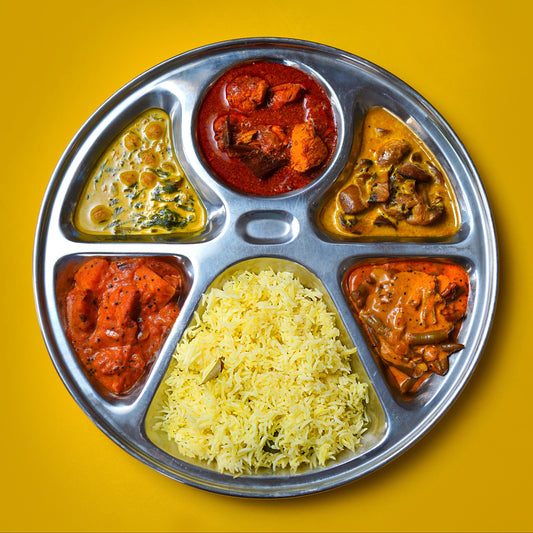 Metallic tray with compartments filled with different types of sri lankan food on a yellow background