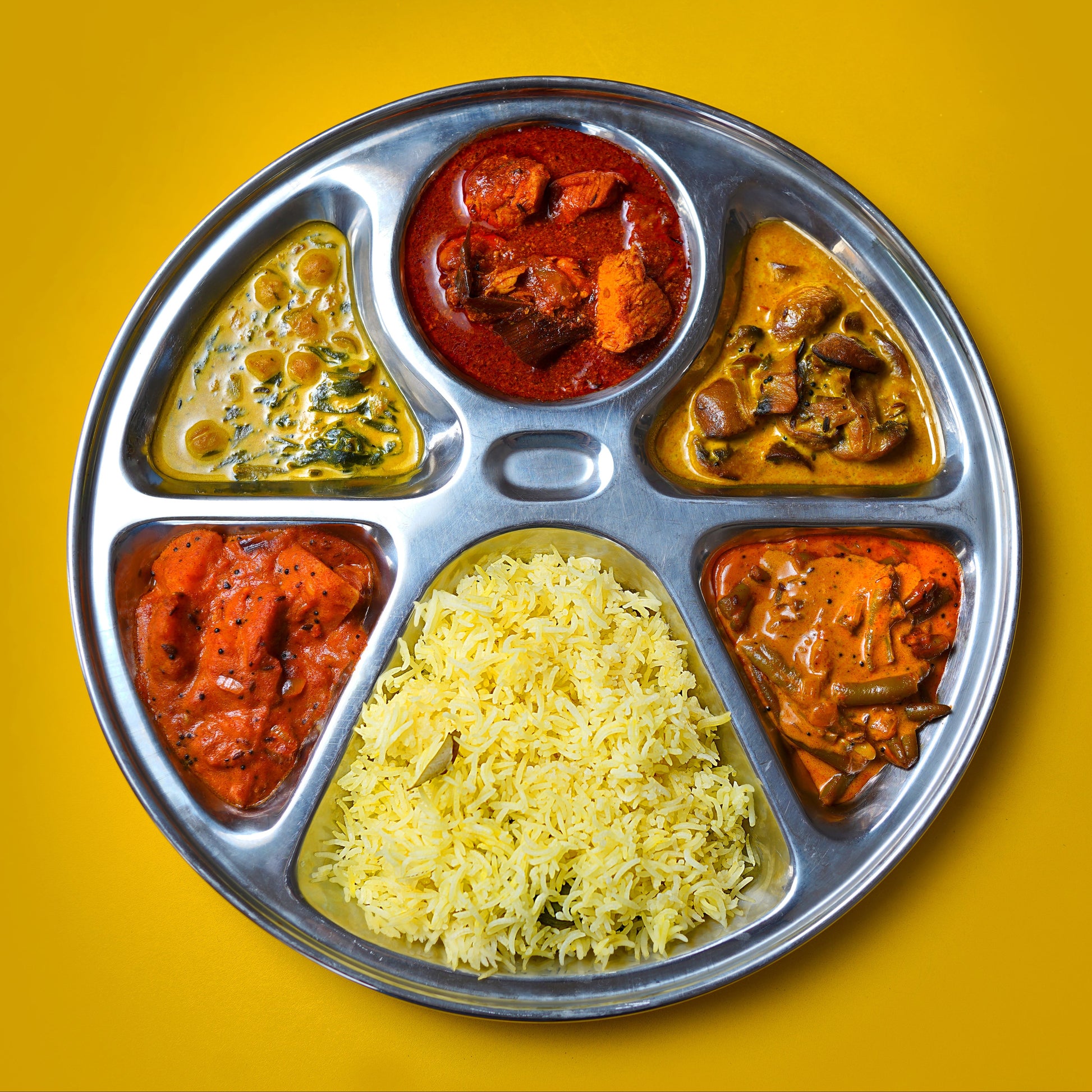 Metallic tray with compartments filled with different types of sri lankan food on a yellow background